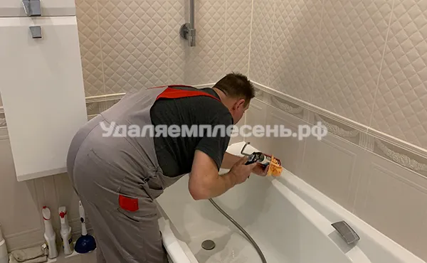 Владимир герметизирует стык между ванной и стеной